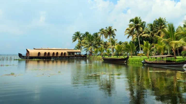 Traditional Kerala houseboat cruising through the calm backwaters of Alleppey surrounded by coconut trees and scenic village landscapes.